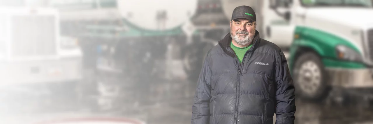 Rhinehart Oil employee posing in a company jacket and cap, and a Rhinehart Oil fuel tanker in the background.