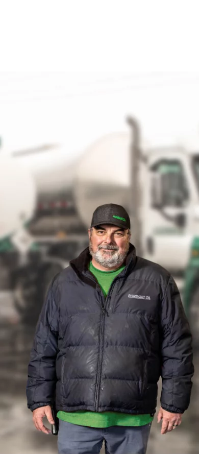 Rhinehart Oil employee posing in a company jacket and cap, and a Rhinehart Oil fuel tanker in the background.