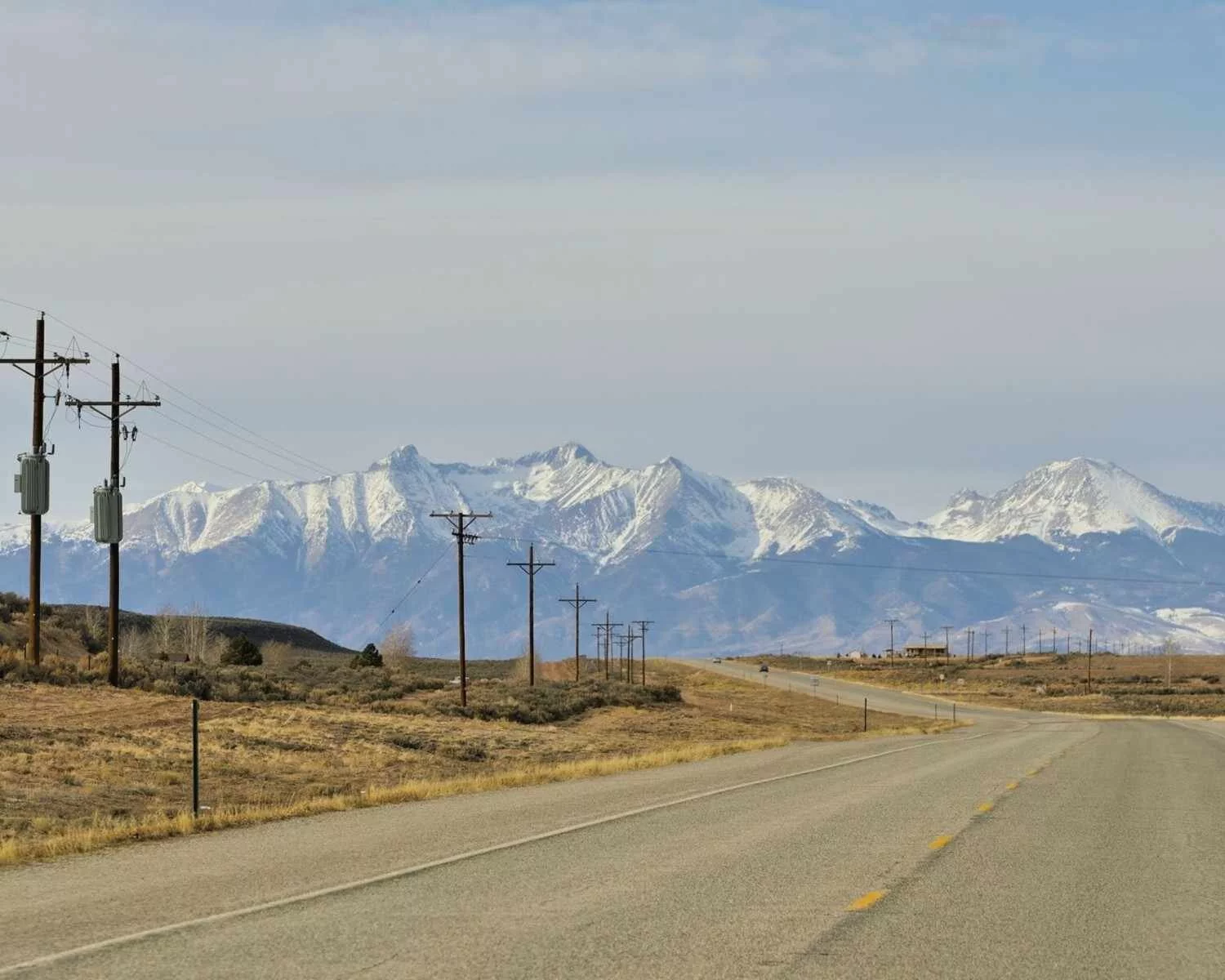 A quiet rural highway in Montana lined with utility poles and backed by snow-covered peaks—representing fuel logistics in remote farm regions.