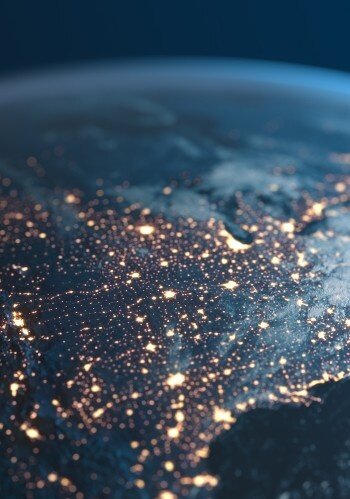 Aerial view of Earth at night, showing glowing city lights across continents and a curved horizon against a dark sky.