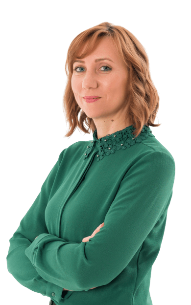 Woman standing with arms crossed, wearing a green blouse, looking confidently at the camera against a plain white background.